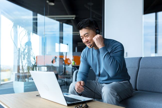 A Taiwanese businessman engages in an informal videoconference call, depicted in a warm, professional setting. He is focused and attentive, with a slight smile, indicating a productive and friendly discussion. The businessman's office is neatly organized, featuring modern technology and a large screen displaying multiple participants, symbolizing the global and interactive nature of the conference. This image captures the essence of contemporary business communication, emphasizing connectivity and cultural diversity in a corporate environment.